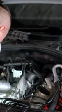 Otomobil tamirhanesi. Tamirci araba motorunu inceliyor. Tamirci araba motoruna ve lambaya bakıyor. Dikey video