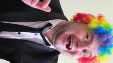 Renkli peruklu dans eden genç bir adam ellerini stüdyo arka planında ritmik olarak hareket ettiriyor. Dikey video.