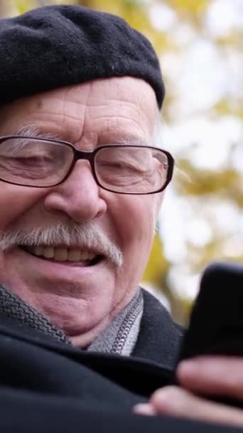 Ένας Γέρος Κάθεται Ένα Παγκάκι Κοιτάζοντας Κινητό Του Και Γελώντας — Αρχείο Βίντεο