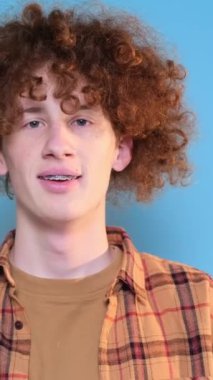 Sıradan tişörtler giyen genç Avrupalı bir adam parmak kaldırıyor. Sade mavi stüdyo arka planında izole edilmiş. Dikey video.