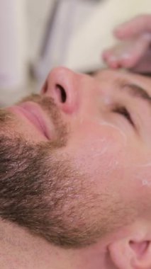 Güzellik uzmanı güzellik merkezinde müşterilerin yüzüne krem sürüyor. Kaplıcadaki yaşlanma karşıtı prosedürler yenileniyor. Dikey video