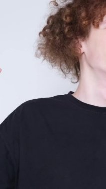 Gülümseyen kıvırcık genç adam beyaz bir arka planda dans ediyor elleriyle hareket ediyor, ellerini kaldırıyor. Dikey video.