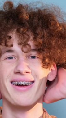 Kıvırcık saçlı bir adam stüdyoda mavi arka plandaki kameraya bakıyor. Dikey video.