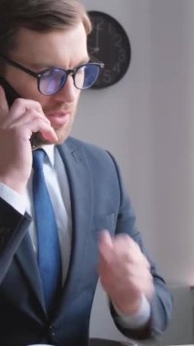 Gözlüklü bir işadamı telefonda konuşuyor, elinde dizüstü bilgisayarla masada oturuyor. Arkadaş canlısı bir yönetici müşteriye telefonla tavsiye eder. Dikey video