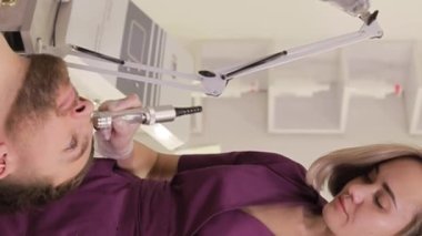 Bir dermatolog, bir sağlık merkezinde bir adamın yüzüne yaşlanma karşıtı ultrason uygular. Dikey video.