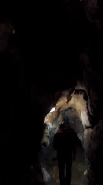 Profesyonel bir mağara bilimci karanlık bir mağarayı aydınlatır ve araştırır. Dikey video.