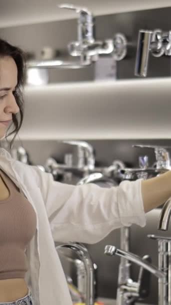 キッチンプランニング 若い女性主婦が台所の蛇口を選びました 女性は現代のハードウェアストアで台所のシンクの蛇口を買う バーティカルビデオ — ストック動画