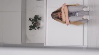 Morali bozuk bir kadın yerde oturuyor ve başını tutuyor. Ailede sorunlar var. Dikey video.