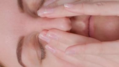 Genç bir kadın elini başının yanında tutuyor ve şiddetli bir baş ağrısı hissediyor. Kapatın. Genç bir kadın kendini iyi hissetmiyor ve evinde baş ağrısı çekiyor. Dikey video.