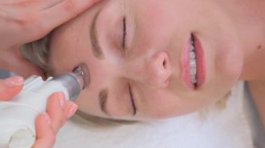 Bir kadının kozmetik güzellik kliniğinde yüz derisi soyma tedavisi görürken yakın çekimi. Hidra elektrikli süpürge. Deri dökülmesi, gençleşme ve su kaybı. Dikey video.
