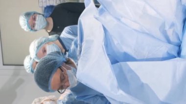 Bir doktor ve asistanlar yaşlı bir kadını ameliyat ediyorlar. Cerrahi operasyondaki öğrenciler. Dikey video.