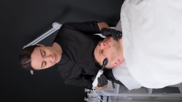 一位专业的美容师用超声波洗掉了一个年轻人脸上的粉刺和伤疤 垂直录像 — 图库视频影像