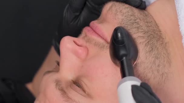 在美容院接受射频整容的大胡子男子的特写镜头 男人接受年轻的面部整容 面部按摩和皮肤护理 垂直录像 — 图库视频影像