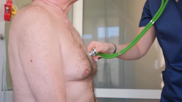 女性の心臓専門医は 古い灰色の髪型の年金受給者の胸に ステスコープを付ける 病院での診察 ハートリズム — ストック動画