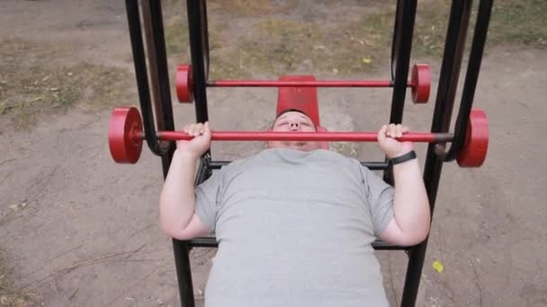 Ein Hartnäckiger Dicker Mann Stemmt Gewichte Liegen Auf Outdoor Trainingsgeräten — Stockvideo