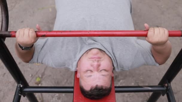Homem Gordo Uma Camiseta Cinza Levanta Pesos Enquanto Está Deitado — Vídeo de Stock