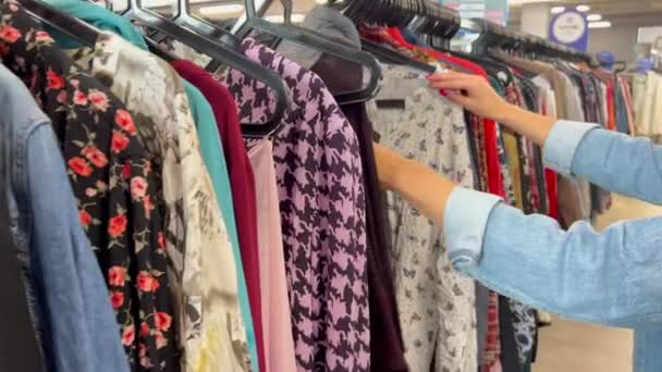 漂流店でハンガーに使用された服を選択する女性の手のクローズアップ 貧困について ヨーロッパおよびアメリカからの使用された衣服 — ストック動画