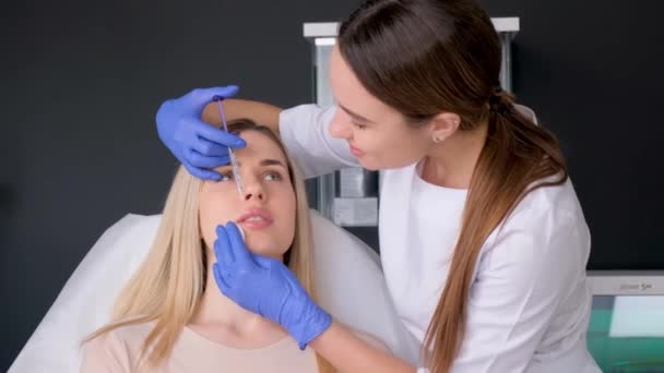 診療所の若い女性に唇注射をする医師 コスメティック手術 彼女の唇のためのボトックス手順を受け取る化粧室の美しいクライアント — ストック動画