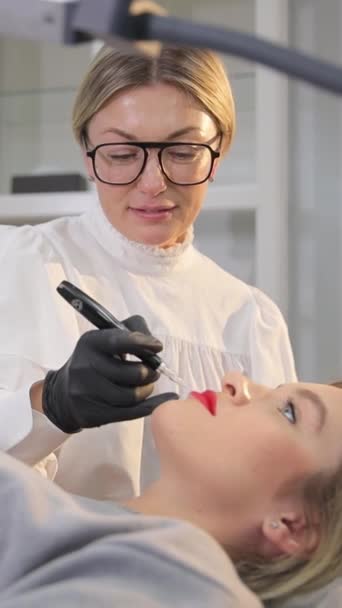 一个戴黑色手套的女性美容师用纹身机在女人的唇上做永久的妆容 微浸渍工艺 — 图库视频影像