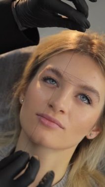 Kaşlardan istenmeyen kılları bir iplikle almak, bir kozmetolog yapar, dikey video..