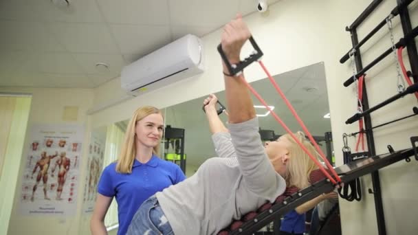 高齢の女性は 負傷後のリハビリテーションコースの一環としてピラティス機の演習を伸ばしています 物理療法の概念 — ストック動画
