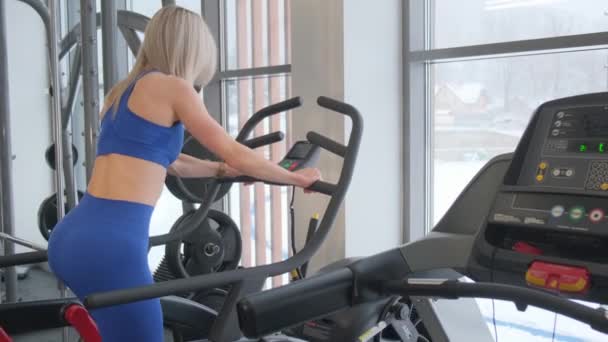年轻的女运动员在健身房的椭圆形机器上锻炼 倒立着 做有氧运动 穿着运动服和紧身衣 — 图库视频影像