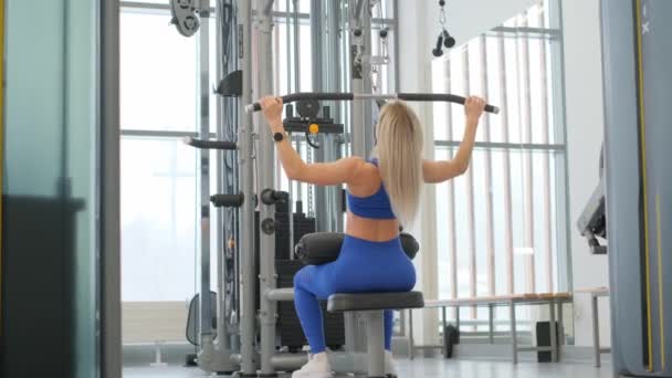 身穿运动服的年轻健身女士正坐在练习机上做举重运动 自律和动机的概念 背肌非常紧张 — 图库视频影像