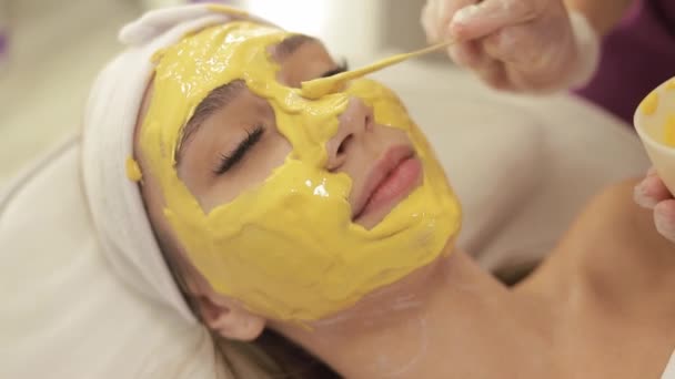 Kosmetolog Stosuje Żółtą Złotą Maskę Alginianową Szpatułką Twarzy Kobiety Zabieg — Wideo stockowe