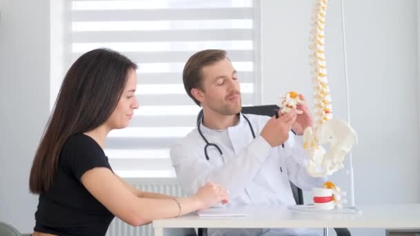 女病人在医生办公室会诊时 与医生谈论她的背部问题 在医务室向病人展示脊柱模型的理疗师 — 图库视频影像