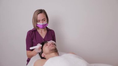 Bir güzellik uzmanı lazer kullanarak bir adamın yüzündeki deriyi temizler. Bir adamın modern kozmetik salonunda bir prosedürü vardır..