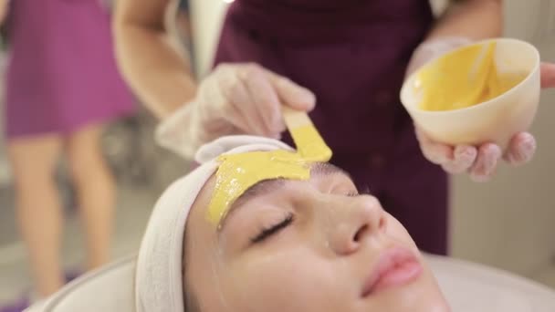 化粧品のスペシャリストは ブラシを使用して金のフェイシャルマスクを適用し 肌を水和させ 輝きと肌に直面させます クローズアップ — ストック動画