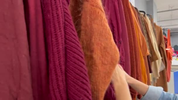 Молодая Длинноволосая Женщина Выбирает Подержанную Одежду Красная Блузка Подержанном Магазине — стоковое видео