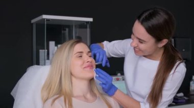 Güzellik salonundaki bir kadın yanağından botoks yaptırıyor, yakın plan. Tıbbi eldiven giyen bir doktor yanağına hyaluronik asit enjekte ediyor..