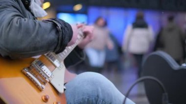 Kalabalık bir şehirde, kot pantolonlu bir adamın rock gitar çalarkenki yakın çekimi. Bir gitarist bir süpermarketin yanında sokakta solo çalıyor.