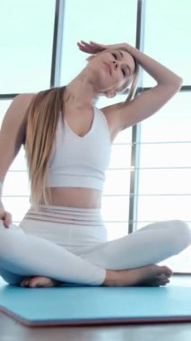Bir kadın yoga minderinde otururken boynunu uzatıyor, eklem ve kas esnekliğine odaklanıyor..