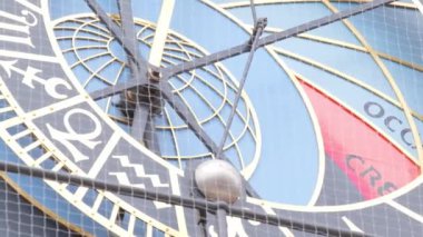 Çemberinde zodyak işareti olan bir saatin yakın çekimi, elektrik mavisi gökyüzüne karşı dizilmiş, bir çemberdeki ağaca benzeyen bir desen yaratıyor..