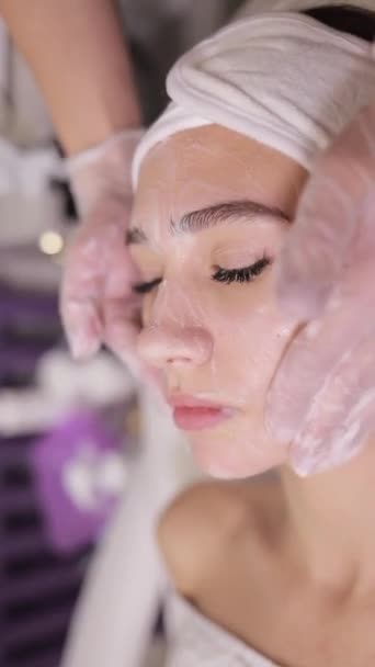 美容師は 若返りのための女性の顔の皮膚にクリームマスクをマッサージします 美容スパサロンでのアンチエイジングスキンケア化粧品手順 クローズアップ バーティカルビデオ — ストック動画