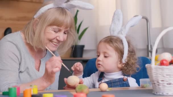 高齢の女性と小さな少女は喜んでイースターの卵を一緒に塗り 楽しい瞬間を共有し 幸せの思い出に残るスナップショットを作成します — ストック動画