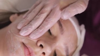 Genç bir kadın güzellik salonunda kozmetik cilt bakımı ve tedavi görüyor. Spa kozmetolojisi ve sağlık rahatlama konsepti. Cilt bakımı. Dikey video