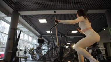 Bir kadın spor aletleri kullanıyor, egzersiz bisikleti, eğlence ve eğlence için müzik dinlerken spor salonunda..