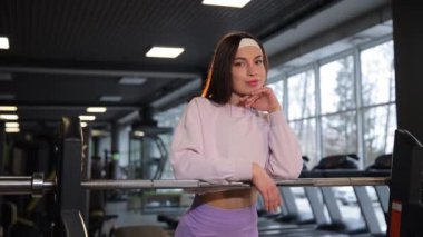 Bir kadın camlarla çevrili spor salonundaki koşu bandını kullanıyor. Camdan şehir binalarına bakıyor..