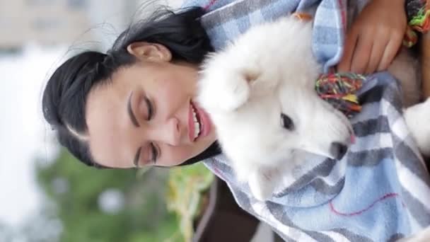 一个快乐的女人抱着一只白色的小狗 它属于斯皮兹犬 裹着舒适的毛毯 — 图库视频影像