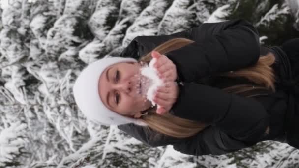 一个戴着帽子的女人把雪从手中吹走 在寒冷的雪地里享受着闲暇和娱乐 — 图库视频影像