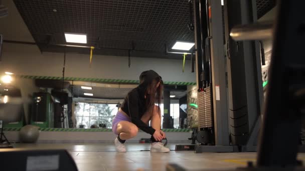 一个女人蹲在一个有木制地板的健身房里 用一台机器进行着锻炼 — 图库视频影像