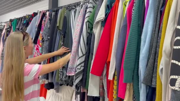 Μια Γυναίκα Εξετάζει Ρούχα Μια Σχάρα Συμπεριλαμβανομένων Των Κλωστοϋφαντουργικών Ειδών — Αρχείο Βίντεο