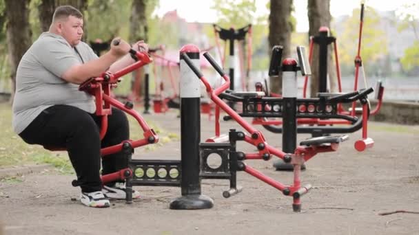 Człowiek Nadwagą Ćwiczący Zewnętrznym Symulatorze Ćwiczący Ramię Grubas Trenuje Ramiona — Wideo stockowe