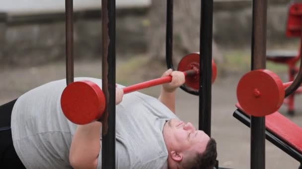 Ein Hartnäckiger Dicker Mann Stemmt Gewichte Liegen Auf Outdoor Trainingsgeräten — Stockvideo