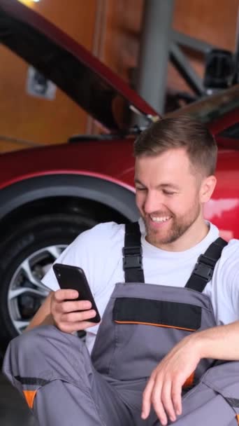 Een Man Zit Bij Een Rode Auto Verdiept Zijn Mobiele — Stockvideo