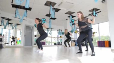 Bir grup kadın spor salonundaki spor eğlencelerinin bir parçası olarak halterleriyle dinamik bir çömelme egzersizi yapıyorlar..
