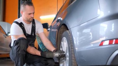 Bir adam garajdaki bir aracın lastiğini değiştiriyor. Arabanın kaputunun yanındaki lastik üzerinde çalışıyor..